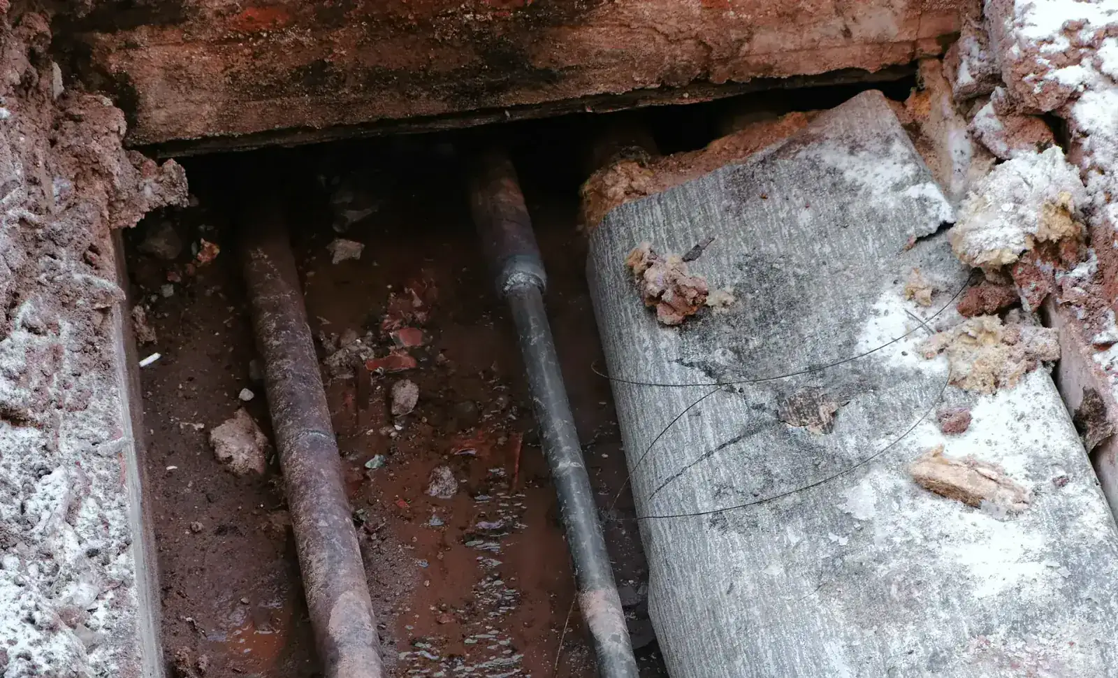 Corroded water lines exposed beneath a broken-out concrete slab