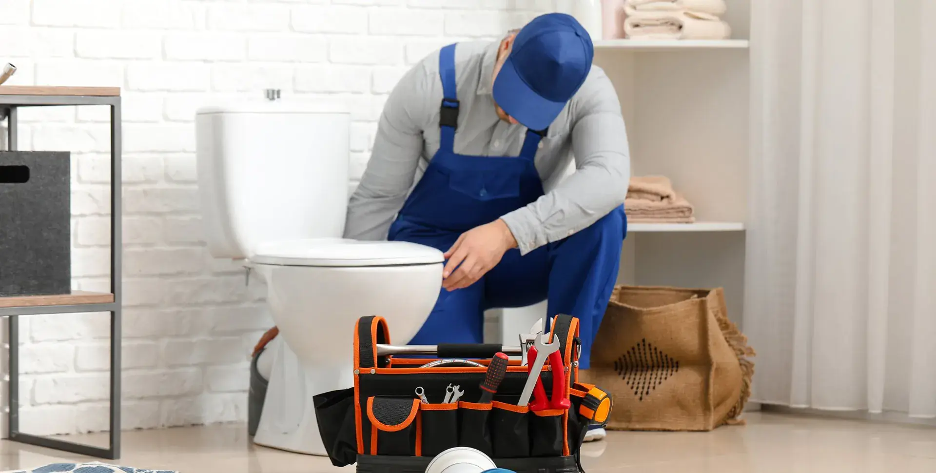 Plumber kneeling beside a toilet with a tool bag, working on a repair